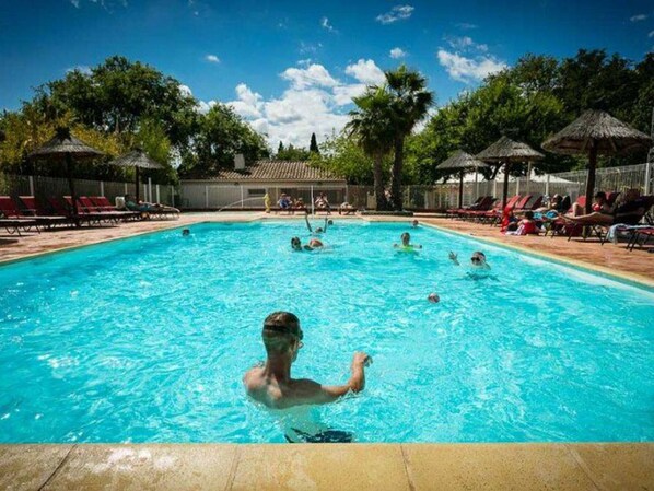 A swimming pool with people in the water, surrounded by lounge chairs and umbrellas.