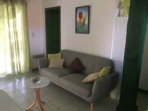 Una sala de estar con un sofá gris, una pequeña mesa redonda, un cuadro de flores y una puerta verde.