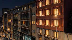 Ett hotell med flera våningar, upplysta fönster, en parkeringsplats och utsikt över gatan.