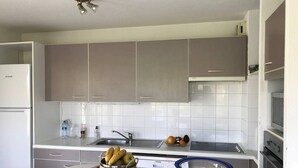 Una cocina funcional con armarios grises, una encimera blanca, un lavamanos y una mesita con un cuenco de fruta.