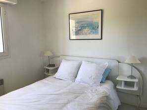 A bedroom with a white bed, two bedside tables with lamps, a framed picture on the wall, and a window on the left. - Apartment with balcony - 4/6 guests (Moliets-et-Maa)