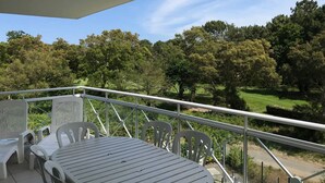 Un balcón con mesa y sillas, con vistas a un paisaje verde con árboles y un campo de golf.