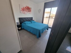 Un dormitorio con cama, mesita de noche, una obra de arte en la pared y vistas a través de una puerta.