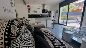 A modern living room with a patterned sofa, a glass coffee table, and a kitchen area with white cabinets and a black countertop. - Spacious house 600m from Empúries beaches with private terrace (L'Escala)