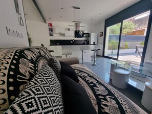 A modern living room with a patterned sofa, a glass coffee table, and a kitchen area with white cabinets and a black countertop. - Spacious house 600m from Empúries beaches with private terrace (L'Escala)