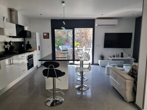 A modern kitchen with a dining area, a sofa, and a TV. - Spacious house 600m from Empúries beaches with private terrace (L'Escala)