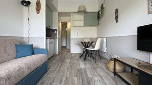Een ruimtelijke leefruimte met een bank, een eettafel met stoelen, een televisie en een keukenhoek.