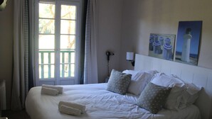 Ett hotellrum med en stor säng, ett fönster med gardiner, en sänglampa och en vägg med en inramad tavla.