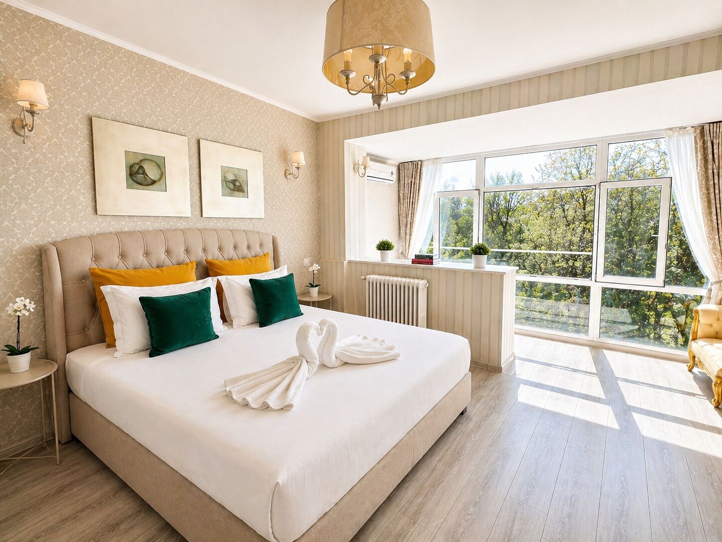 Ruime slaapkamer met een groot bed, een kroonluchter en uitzicht op bomen door het raam.