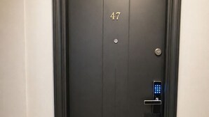 Una puerta de color oscuro con el número 47, un teclado de combinación y un pequeño candado circular en una pared con suelo texturizado.