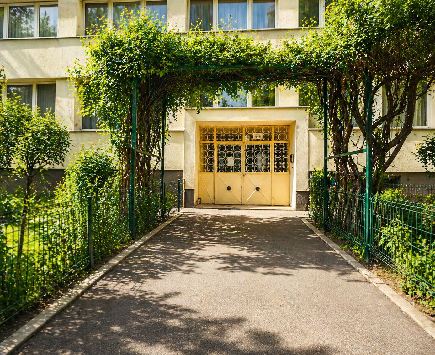 A building entrance with a yellow gate, surrounded by greenery and a paved path.