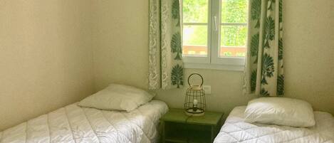 Een kamer met twee eenpersoonsbedden, een kleine tafel met een lamp en een raam met gordijnen.