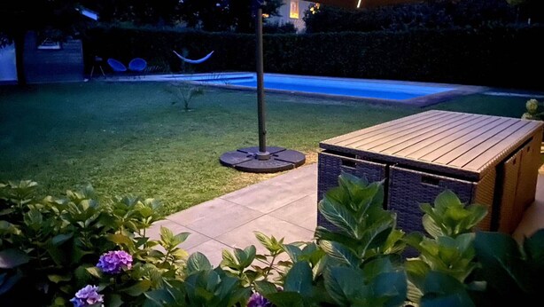 Un espace patio comprenant une table en bois, une table ronde avec des chaises et un grand parasol.