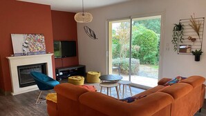 Un salon comprenant un canapé, un téléviseur, une cheminée et une porte-fenêtre coulissante donnant sur un jardin.
