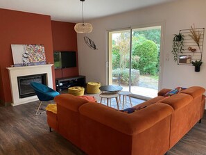 A living room with a sofa, a television, a fireplace, and a sliding glass door leading to a garden. - Villa with pool - 8 guests (Moliets-et-Maa)