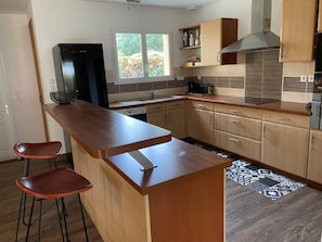 A modern kitchen with a central island, bar stools, a refrigerator, a stove, and a window. - Villa with pool - 8 guests (Moliets-et-Maa)