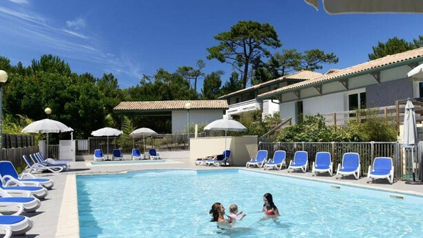 A swimming pool with lounge chairs and umbrellas, surrounded by buildings and trees. - Charming apartment with pool - 6 guests (Moliets-et-Maa)
