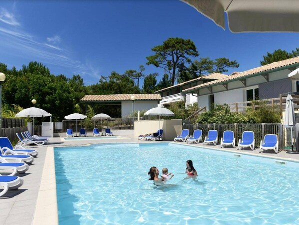 Ein Swimmingpool mit Liegestühlen und Sonnenschirmen, umgeben von Gebäuden und Bäumen.
