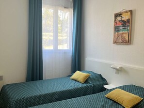A room with two beds, a window with curtains, a wall-mounted picture, and a small table. - Charming apartment with pool - 6 guests (Moliets-et-Maa)