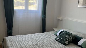 A room with a bed, a window with curtains, a wall-mounted light, and a framed picture. - Charming apartment with pool - 6 guests (Moliets-et-Maa)