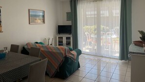A living room with a sofa, TV, dining table, chairs, and a sliding glass door to the outside. - Charming apartment with pool - 6 guests (Moliets-et-Maa)