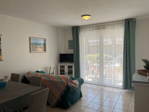 Ein Wohnzimmer mit einer Couch, Fernseher, Esstisch, Stühlen und einer Schiebeglastür nach draußen.