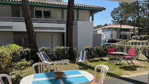A patio with a round table, white chairs with orange cushions, and a blue and white tablecloth. - Charming apartment with pool - 6 guests (Moliets-et-Maa)