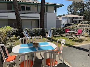 Eine Terrasse mit einem runden Tisch, weißen Stühlen mit orangenen Kissen und einer blau-weißen Tischdecke.