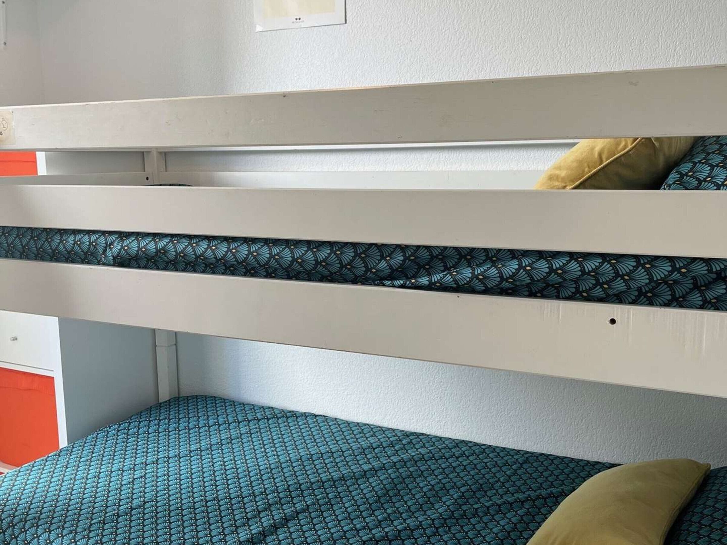 Een stapelbed met een gestreept matras, een kussen en een wandlamp.
