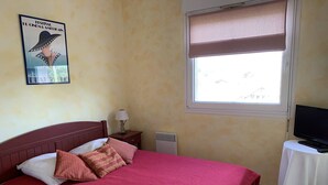 Ein Schlafzimmer mit einem Bett, einem Fernseher auf einem Nachttisch, einem Fenster mit Jalousie und einem Poster an der Wand.
