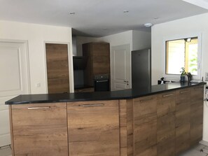 A kitchen with wooden cabinets, a black countertop, and a window with a view. - Villa with heated pool - 6 guests (Moliets-et-Maa)