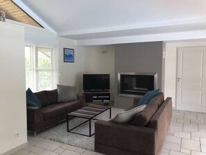 A living room with two sofas, a coffee table, a TV, and a window. - Villa with heated pool - 6 guests (Moliets-et-Maa)