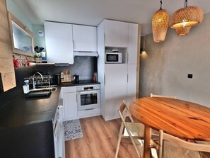 A compact kitchen with white cabinets, a microwave, and a wooden dining table. - Convenient studio, ski-in/ski-out - 4 guests (Le Grand-Bornand)