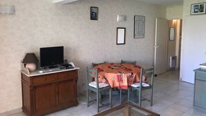 Ein Wohnzimmer mit Fernseher, einer Holzeinrichtung, einem Esstisch mit Stühlen und einer Küche im Hintergrund.