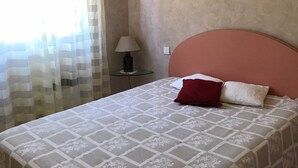 Ein Schlafzimmer mit Bett, Nachttisch, Lampe und einem Fenster mit Vorhängen.