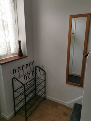 Een kamer met een raam, een spiegel, een metalen rek en een houten bank.