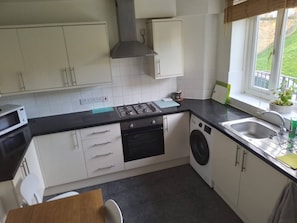 Een compacte keuken met een gasfornuis, oven, magnetron en een ingebouwde wasmachine.