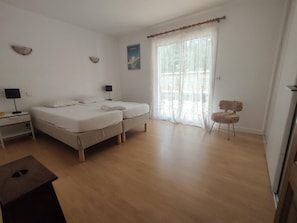 A bedroom with two beds, a chair, a nightstand, a lamp, and a window with sheer curtains. - Renovated house with WiFi - 8 guests (Messanges)