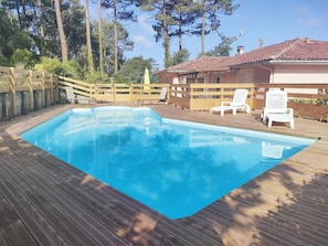 A rectangular swimming pool with a wooden deck, surrounded by a wooden fence and white chairs. - Renovated house with WiFi - 8 guests (Messanges)
