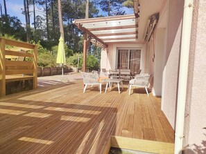 Eine Terrasse im Freien mit Holzboden, weißen Korbmöbeln und einer Pergola mit Lichterketten.
