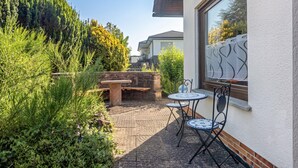 Een terras met een tafel en stoelen, omgeven door groen en een uitzicht op een huis.