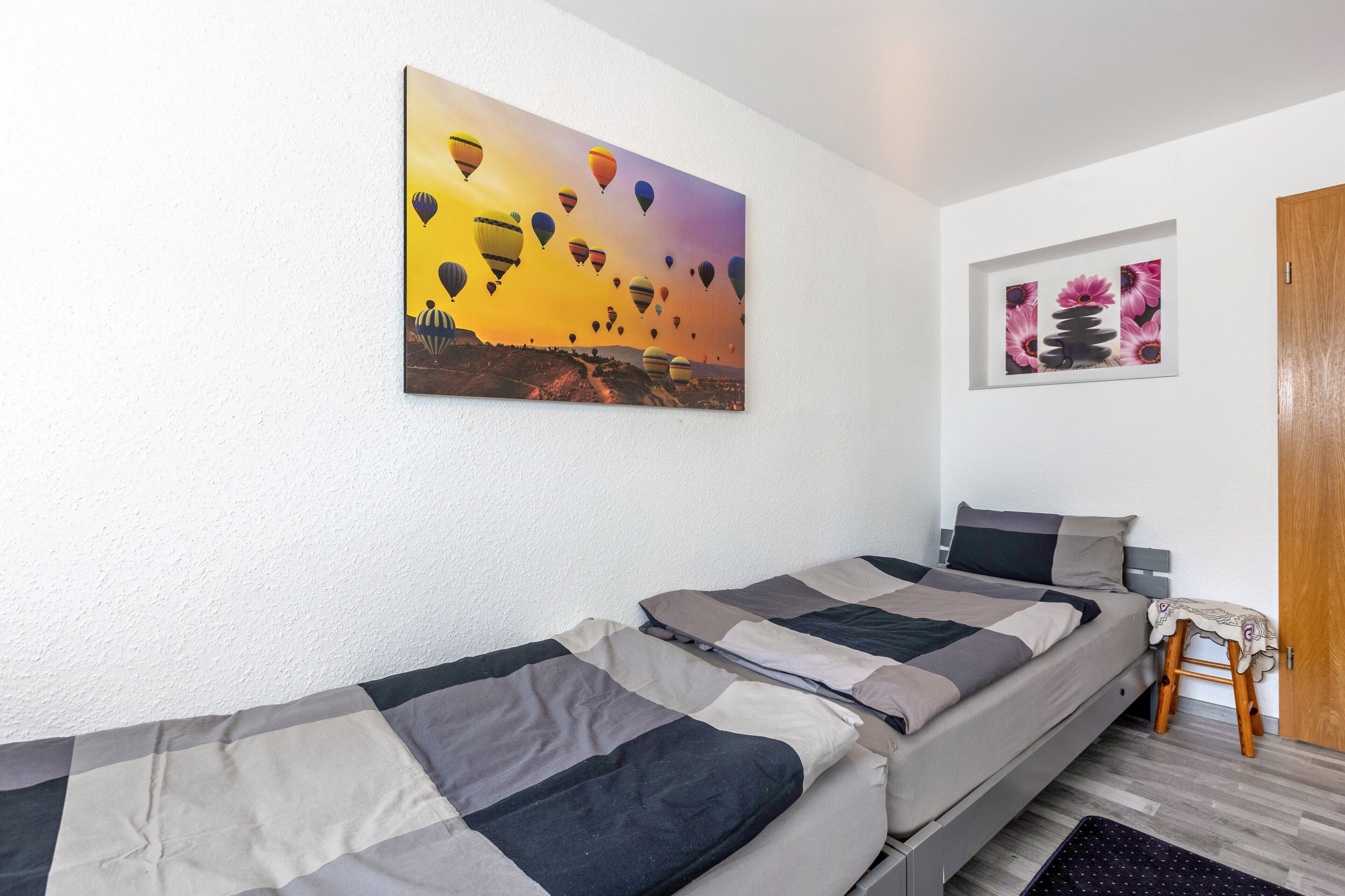 Una habitación con dos camas, un cuadro de globos aerostáticos y una foto enmarco de flores.