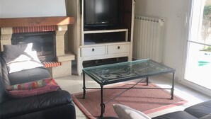 Un salon comprenant un canapé, une table basse avec un plateau en verre, une cheminée et un téléviseur posé sur un meuble.