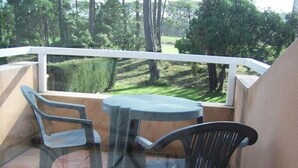 Un balcon avec une table en verre et deux chaises, donnant sur un paysage verdoyant parsemé d’arbres.