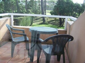 Ein Balkon mit einem Glastisch und zwei Stühlen, mit Blick auf eine grüne Landschaft mit Bäumen.