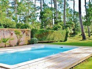 Ein rechteckiger Swimmingpool mit Holzterrasse, umgeben von üppiger Vegetation und hohen Bäumen.