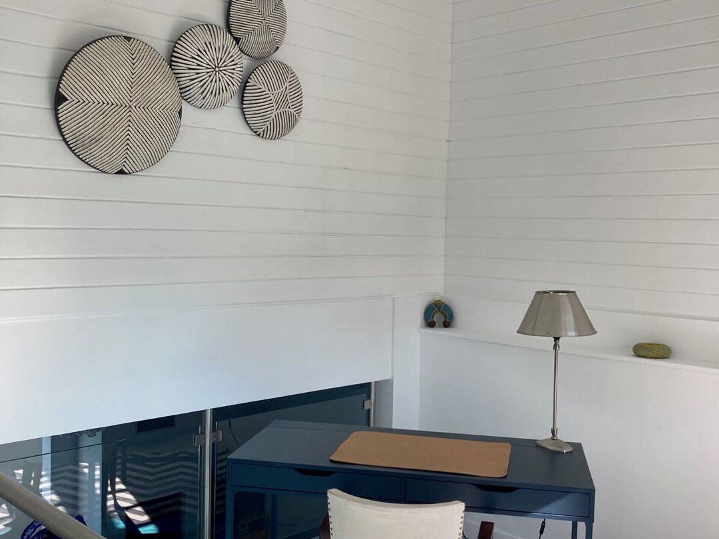 A modern room with a glass desk, a lamp, and decorative wall art.