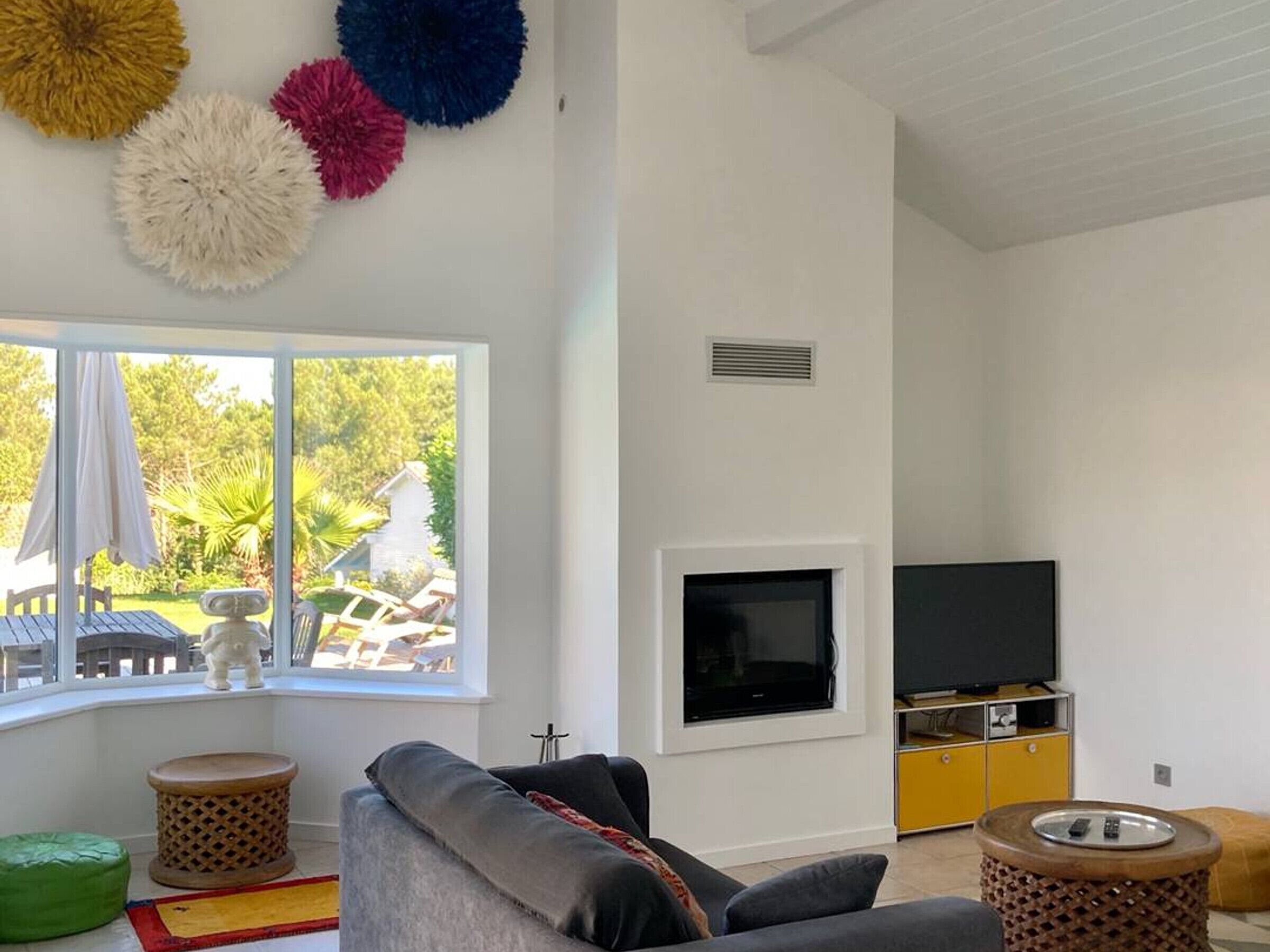 Una sala de estar con sofá, televisor, chimenea y ventana con vista a un jardín.