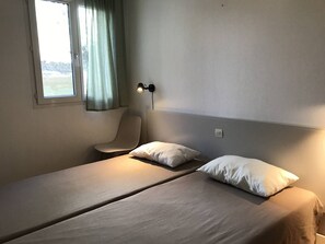 A room with two beds, a chair, a window with curtains, and a wall-mounted lamp. - Apartment with parking, pets allowed - 6 guests (Moliets-et-Maa)