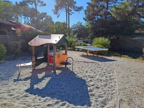 Ein Spielplatz mit einer Kletterkonstruktion und einem Tischtennisschläger in sandigem Gelände.
